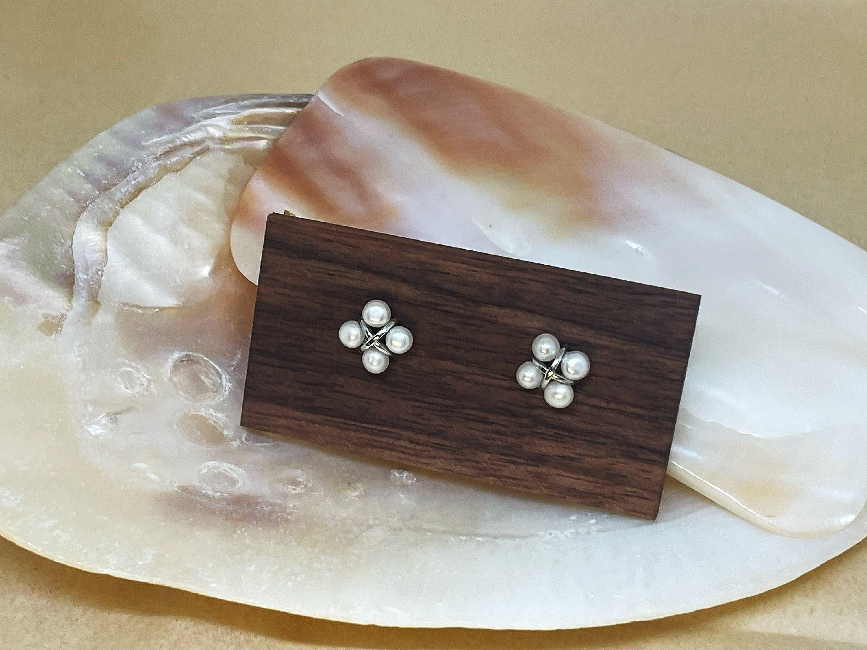 CAELLIA freshwater pearl rhomboid stud earrings displayed on a wooden block over a shell.