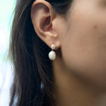 A model wears Caellia 14K gold plated sterling silver earrings featuring two teardrop pearls.