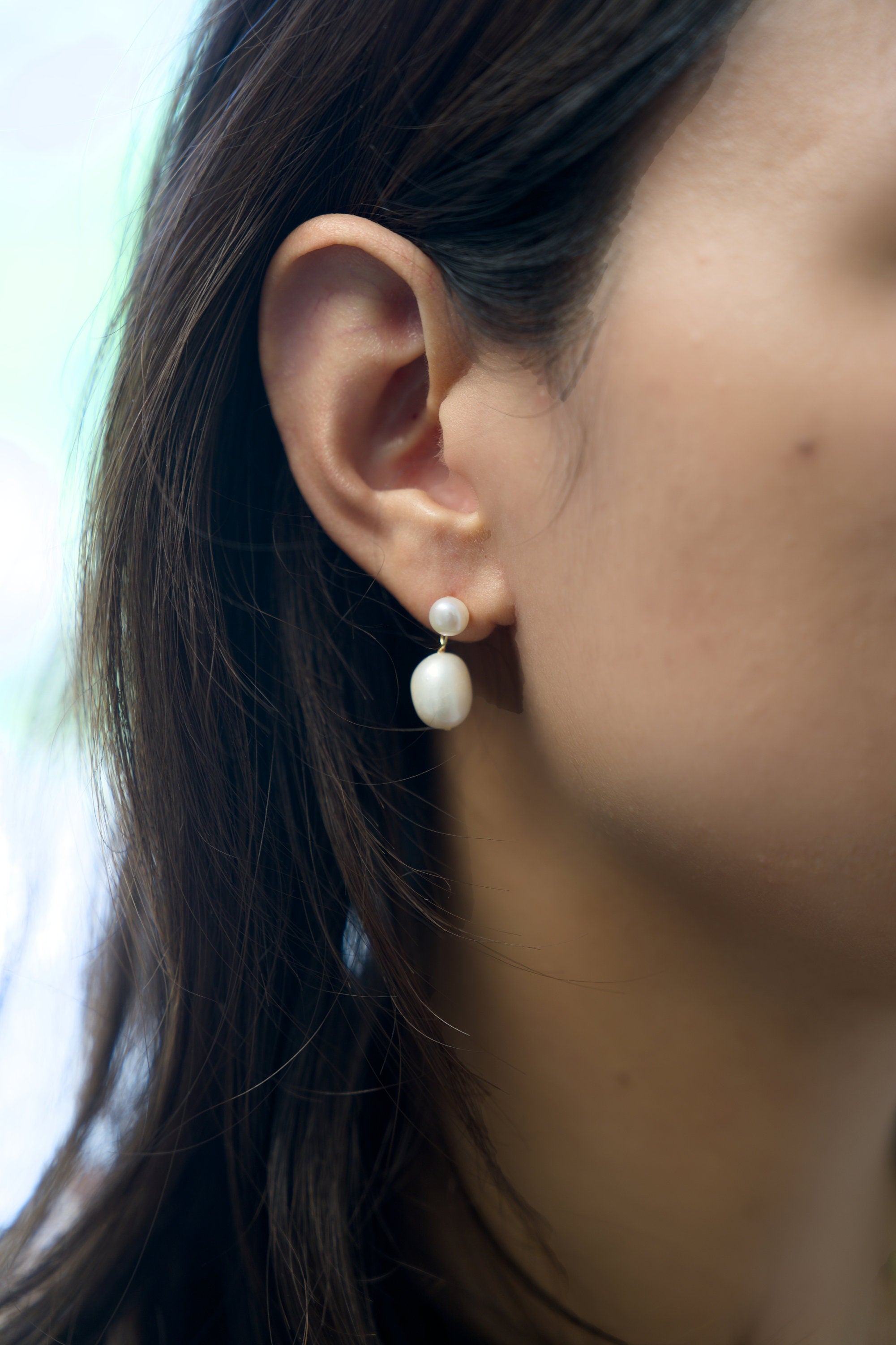A model wears Caellia 14K gold plated sterling silver earrings featuring two teardrop pearls.