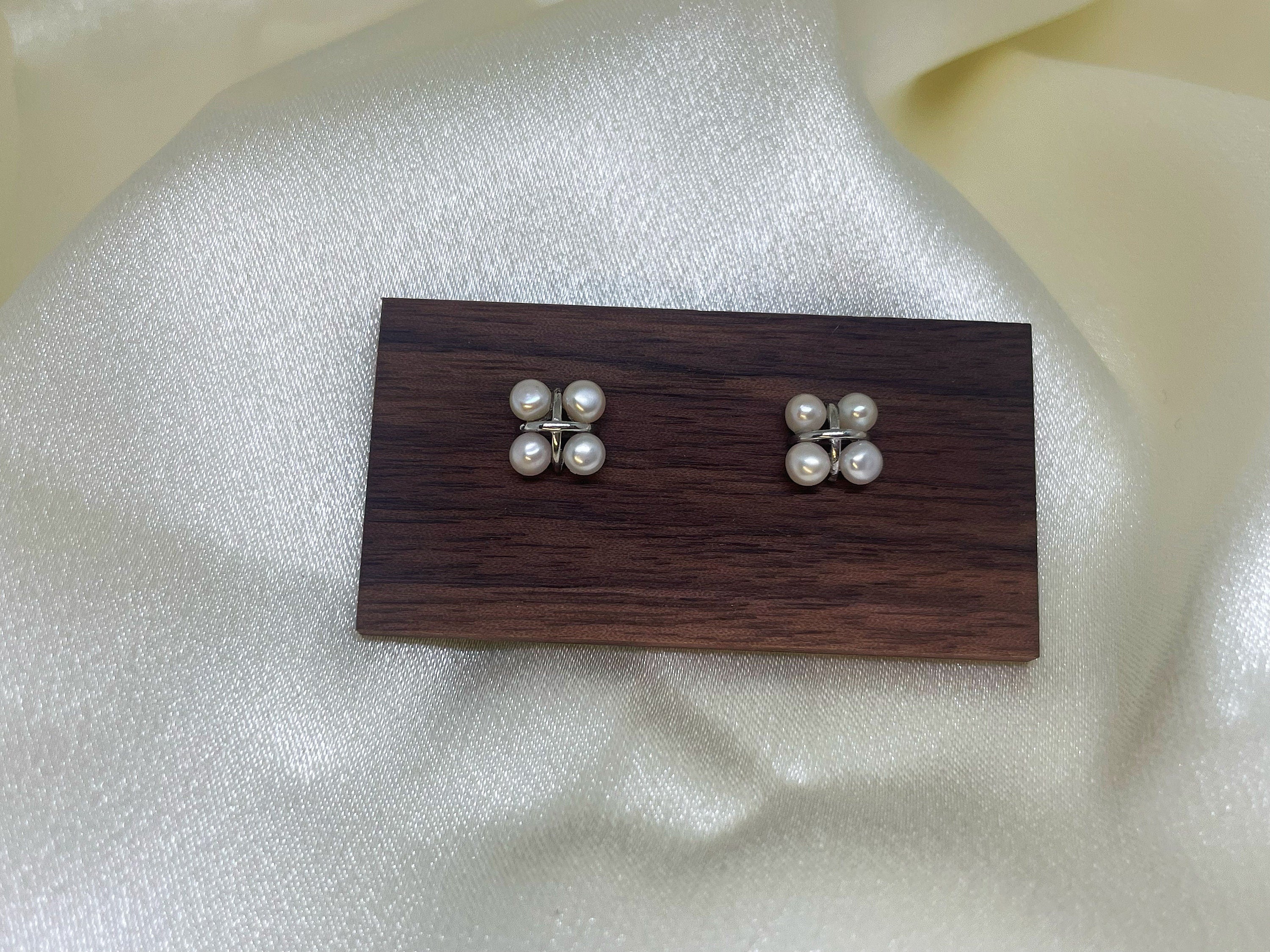 CAELLIA freshwater pearl rhomboid stud earrings displayed on a wooden stand.
