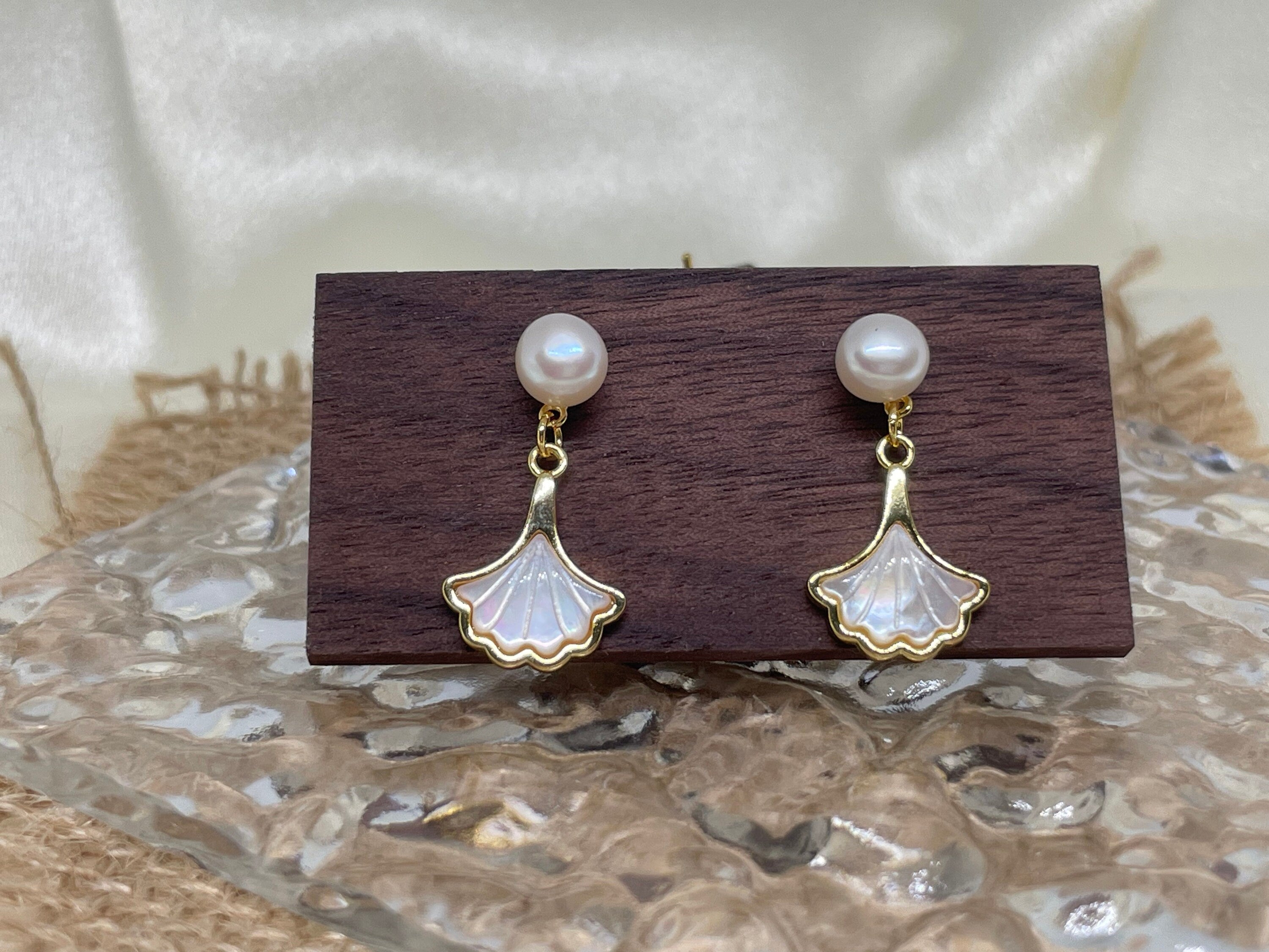 Caellia 14K gold earrings featuring a freshwater pearl stud and a mother-of-pearl fan dangle.