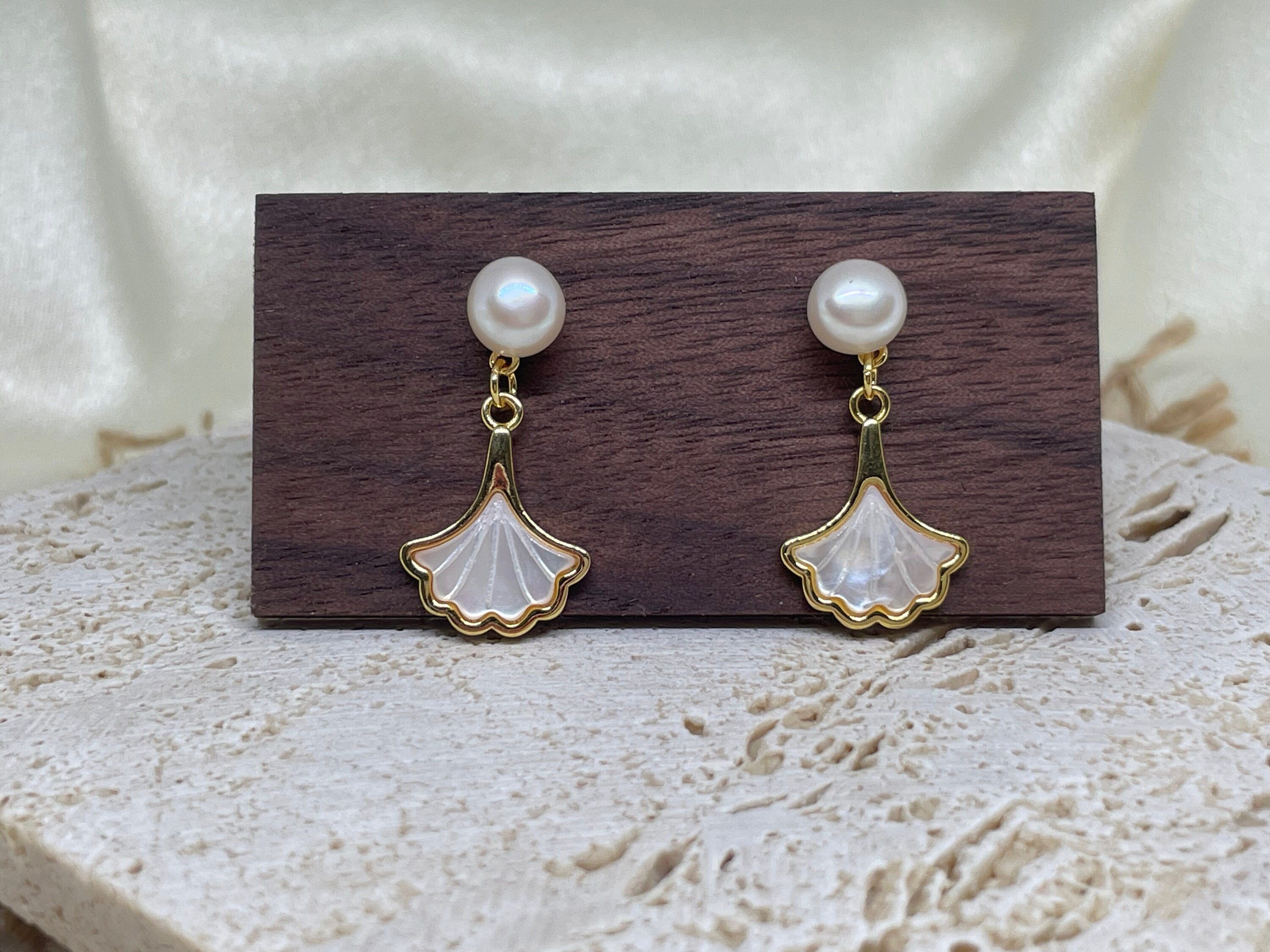 Caellia 14K gold earrings featuring a freshwater pearl stud and a mother-of-pearl fan dangle.