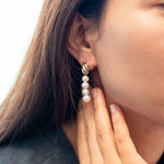 A woman wears a gold earring with four dangling pearls.