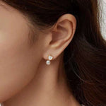 A model wears Caellia 14K gold stud earrings featuring a heart-shaped fritillaria shell and pearl.