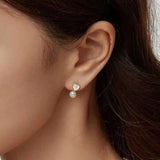 A model wears Caellia 14K gold stud earrings featuring a heart-shaped fritillaria shell and pearl.