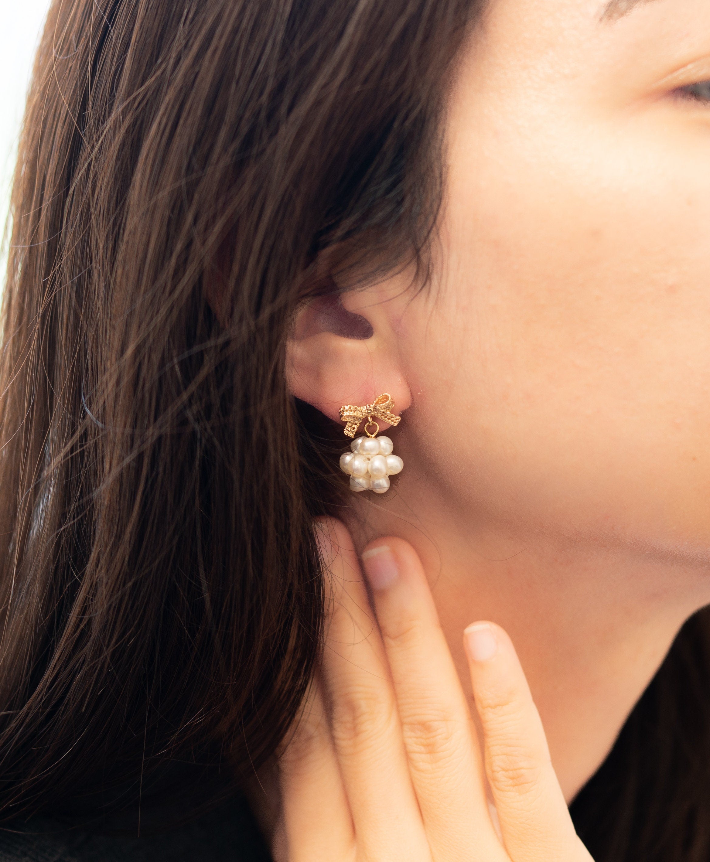 A model wears Caellia 14K gold bowknot earrings featuring a cluster of freshwater pearls.