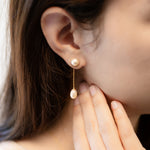 A woman wears CAELLIA gold-plated dangle earrings featuring a round pearl stud and teardrop pearl.