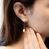 A woman wears CAELLIA gold-plated dangle earrings featuring a round pearl stud and teardrop pearl.