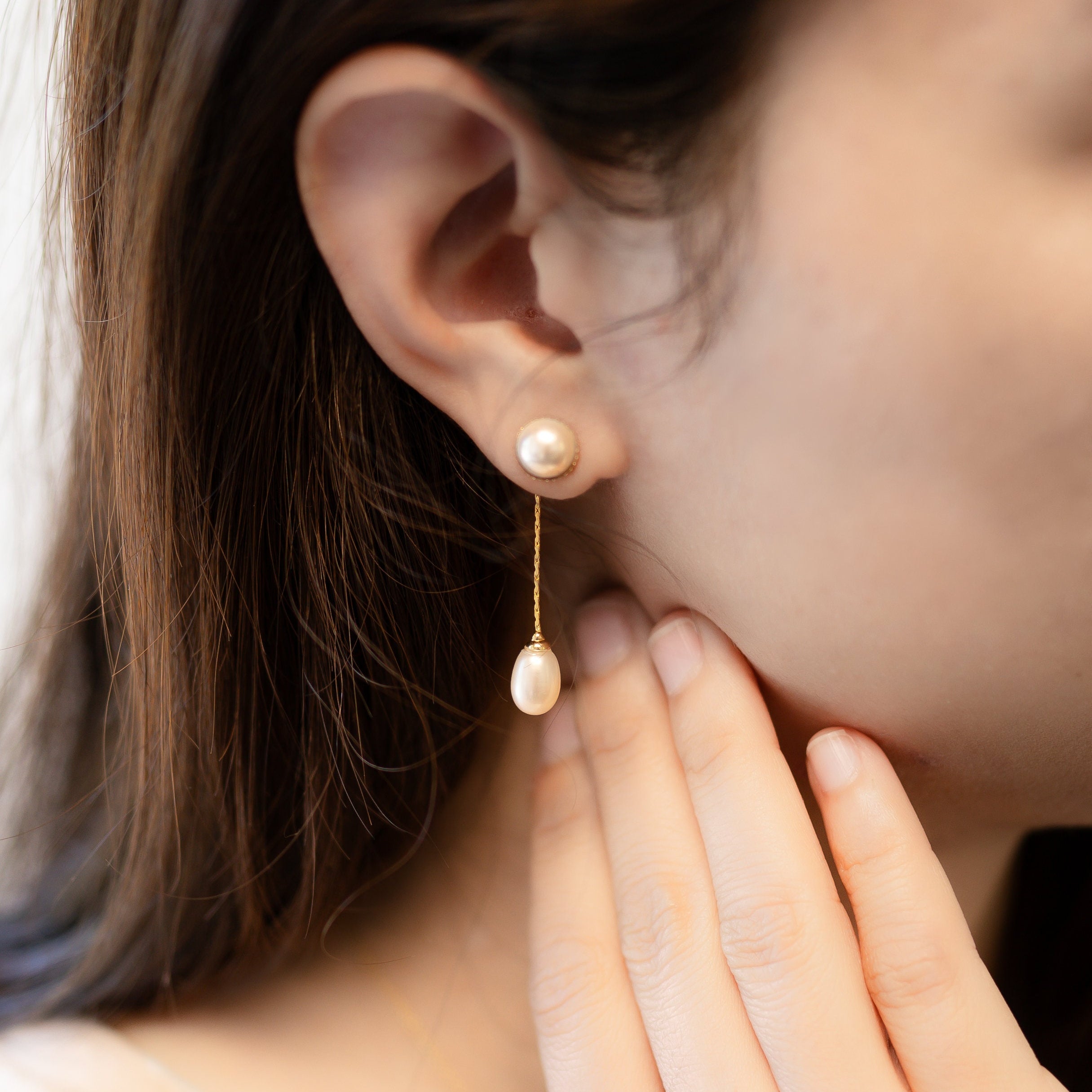 A woman wears CAELLIA gold-plated dangle earrings featuring a round pearl stud and teardrop pearl.