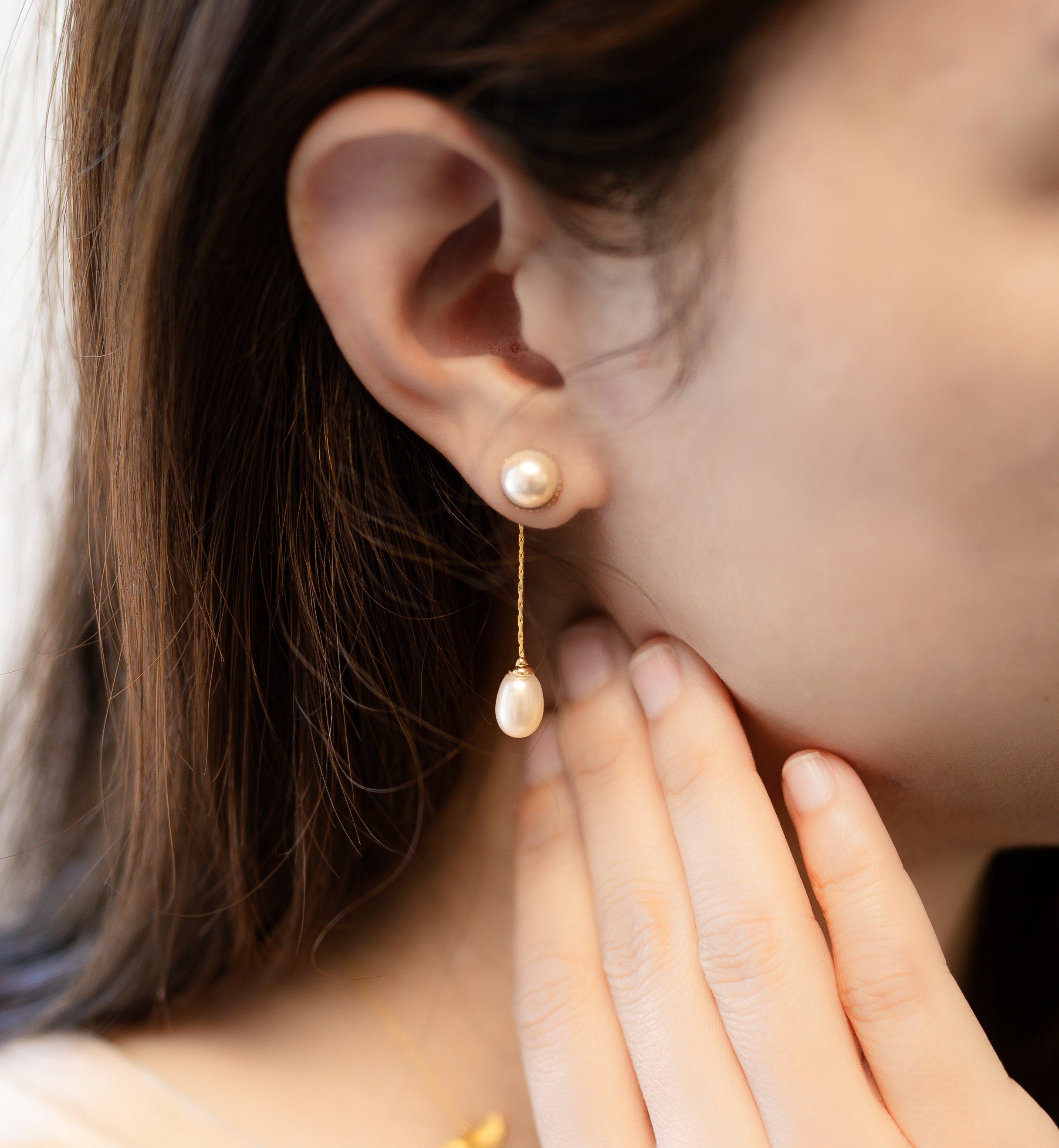 A woman wears CAELLIA gold-plated dangle earrings featuring a round pearl stud and teardrop pearl.