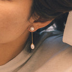 A person wears CAELLIA gold-plated dangle earrings featuring a round pearl stud and teardrop pearl.