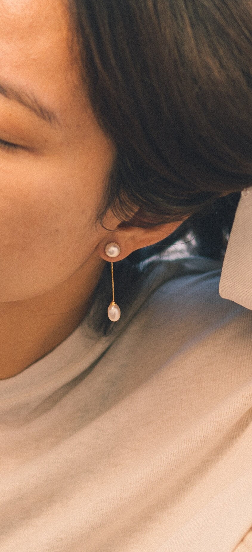 A person wears CAELLIA gold-plated dangle earrings featuring a round pearl stud and teardrop pearl.
