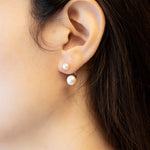 A person wearing Caellia sterling silver double freshwater pearl stud earrings.
