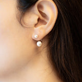 A person wearing Caellia sterling silver double freshwater pearl stud earrings.