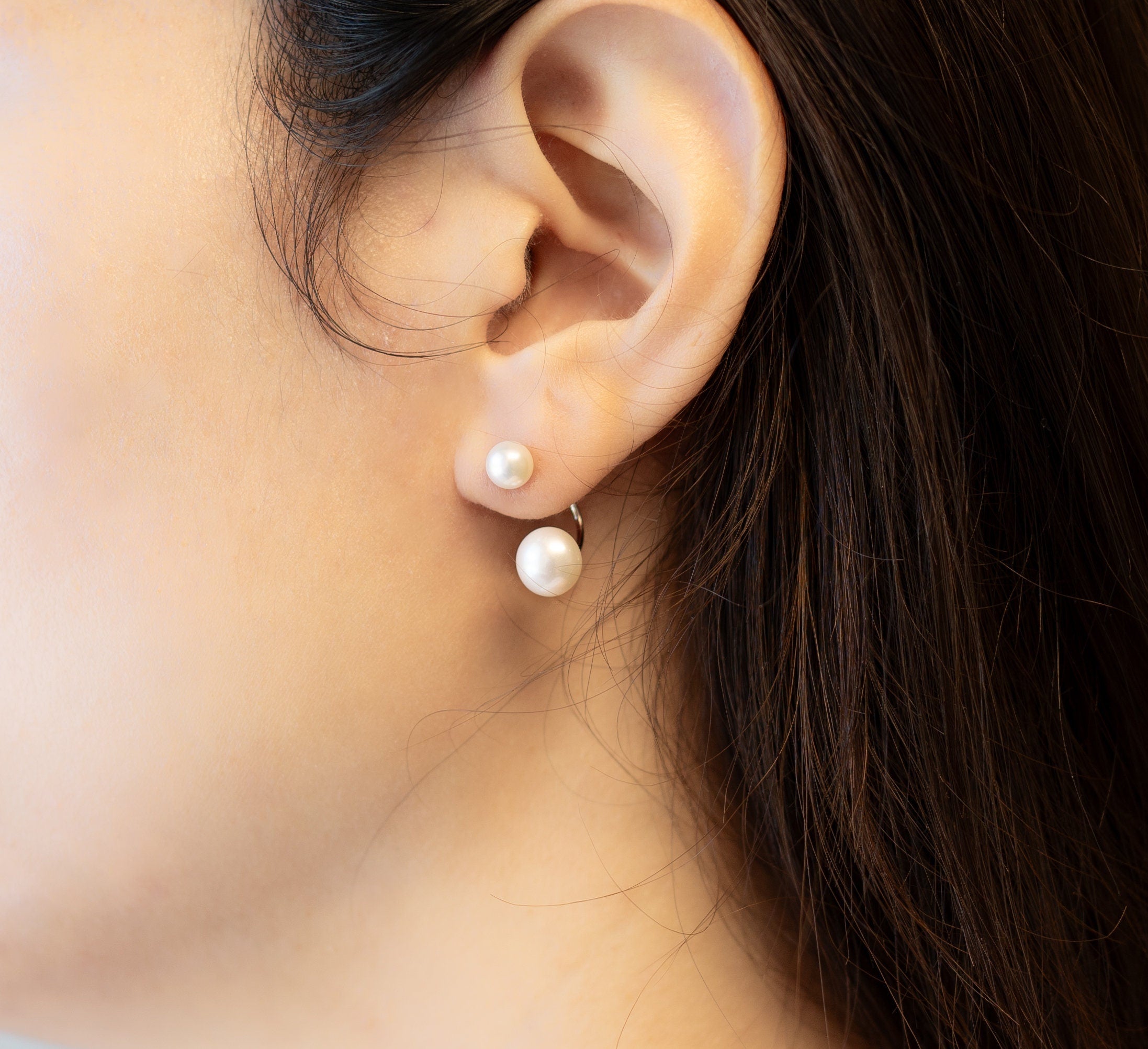 A person wearing Caellia sterling silver double freshwater pearl stud earrings.