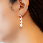 Three pearl drop earrings on a person's ear.