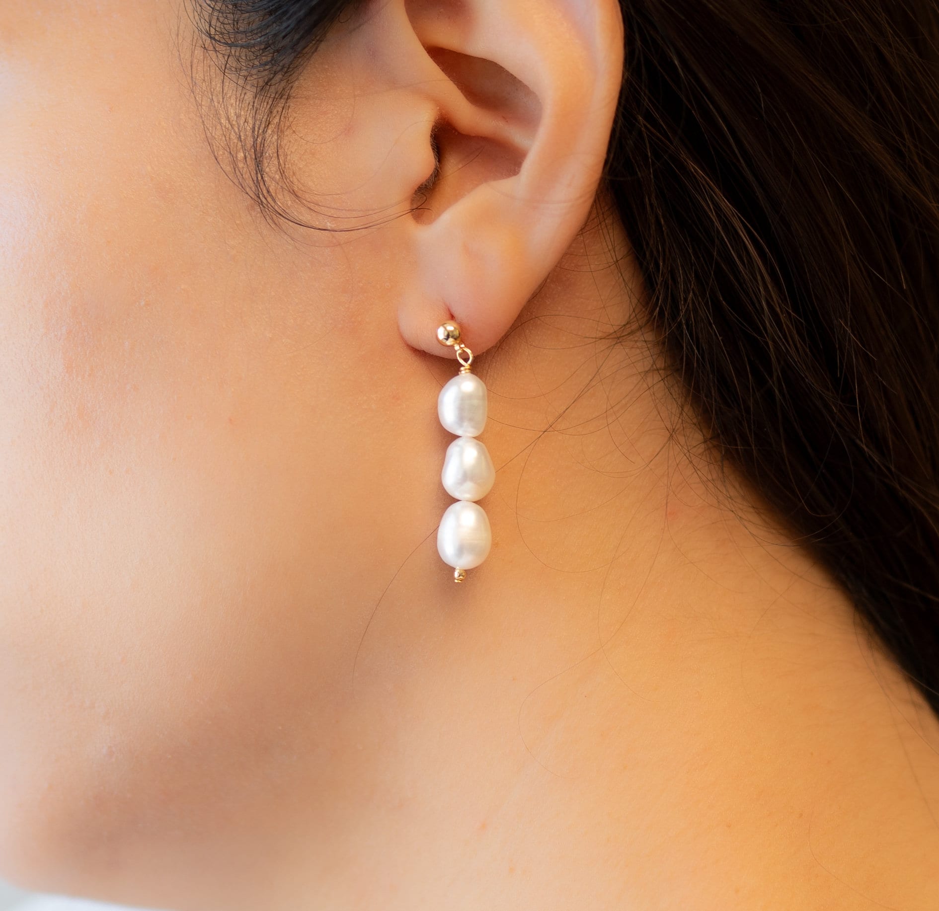 Three pearl drop earrings on a person's ear.