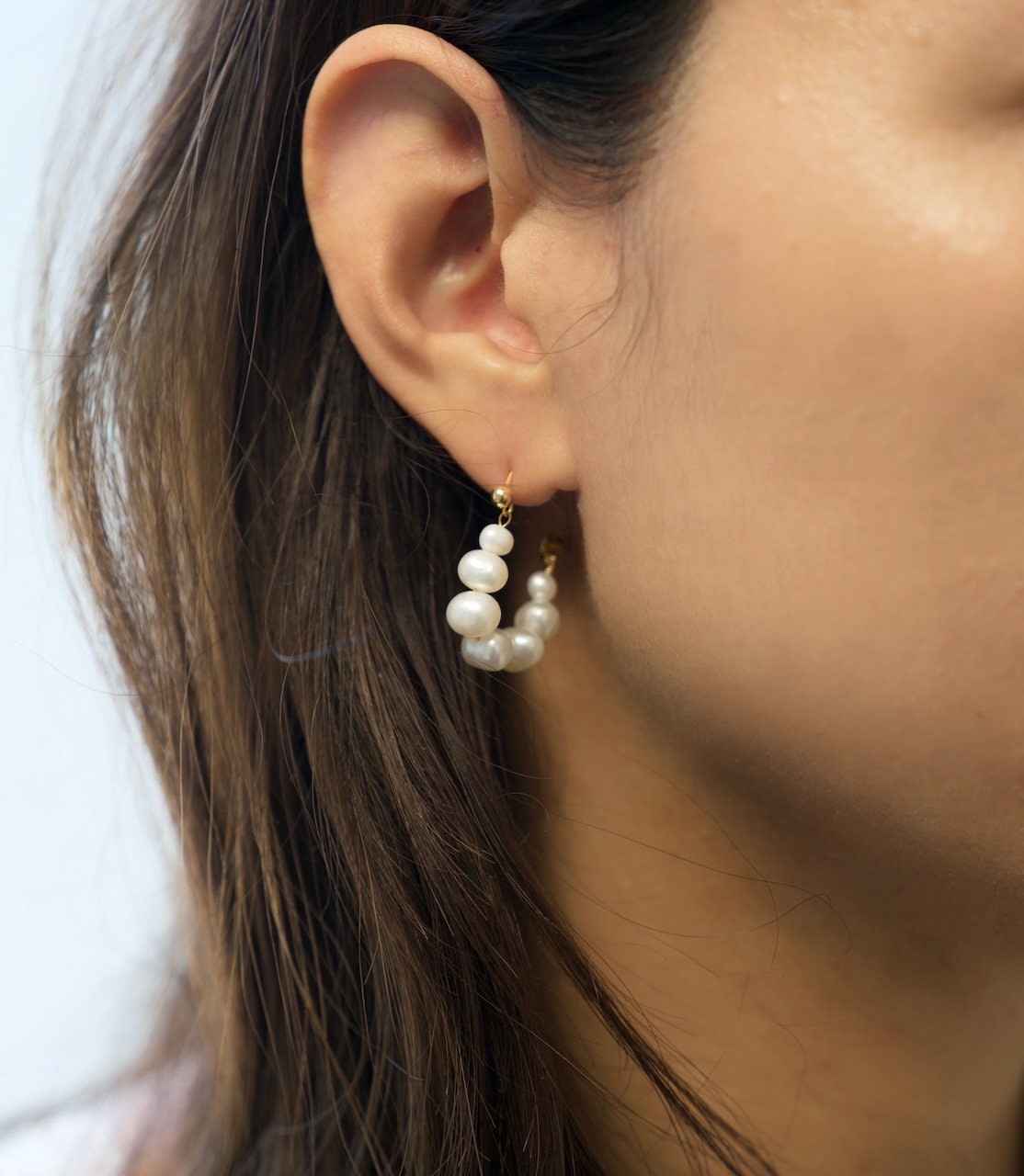 A model wears Caellia 18K gold hoop earrings featuring a row of small freshwater pearls.
