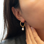 A person wears a Caellia 14K gold twisted hoop earring with a dangling freshwater pearl.