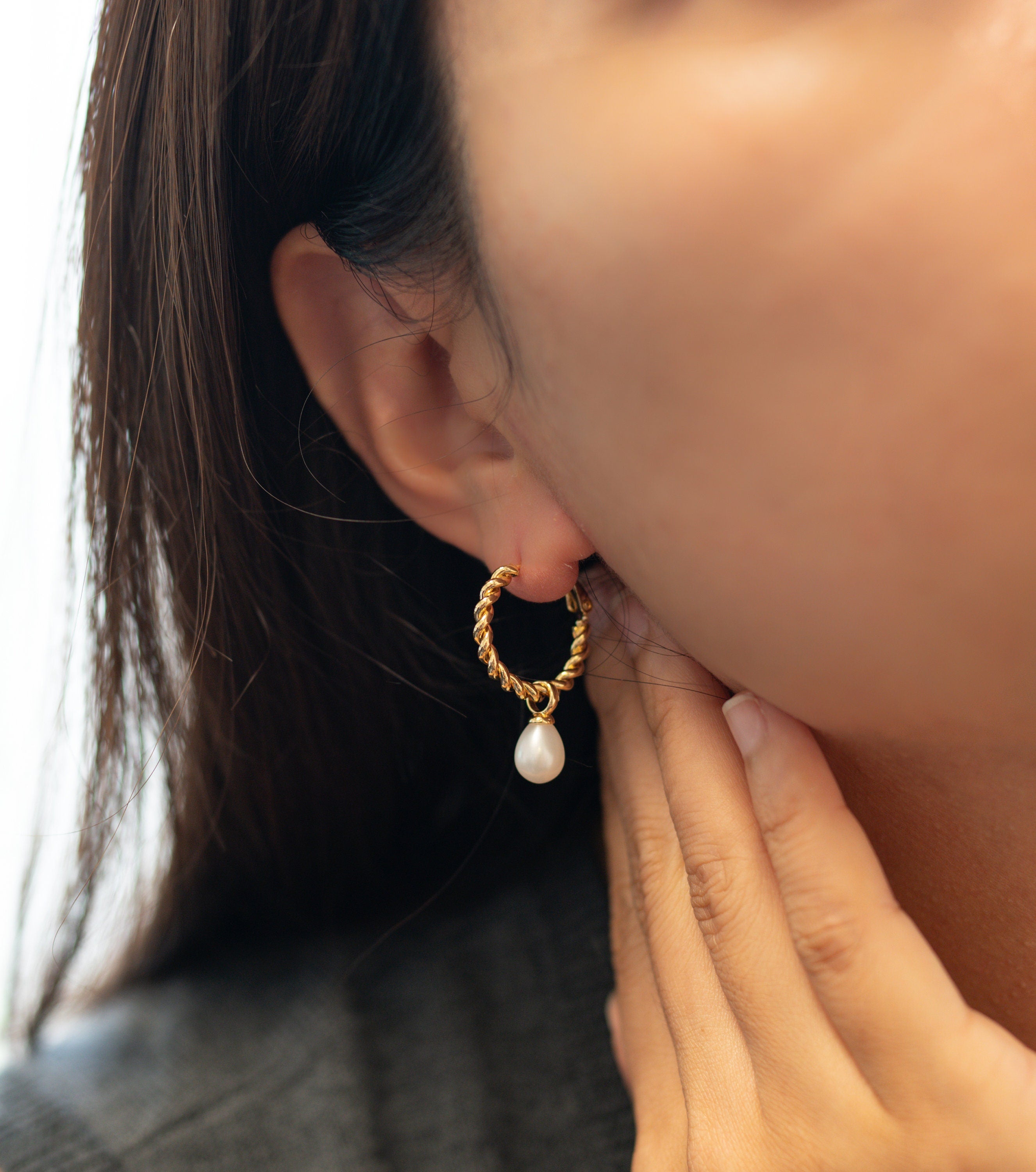 A person wears a Caellia 14K gold twisted hoop earring with a dangling freshwater pearl.