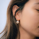 A woman wearing Caellia 14K gold bowknot earrings with dangling freshwater pearl clusters.