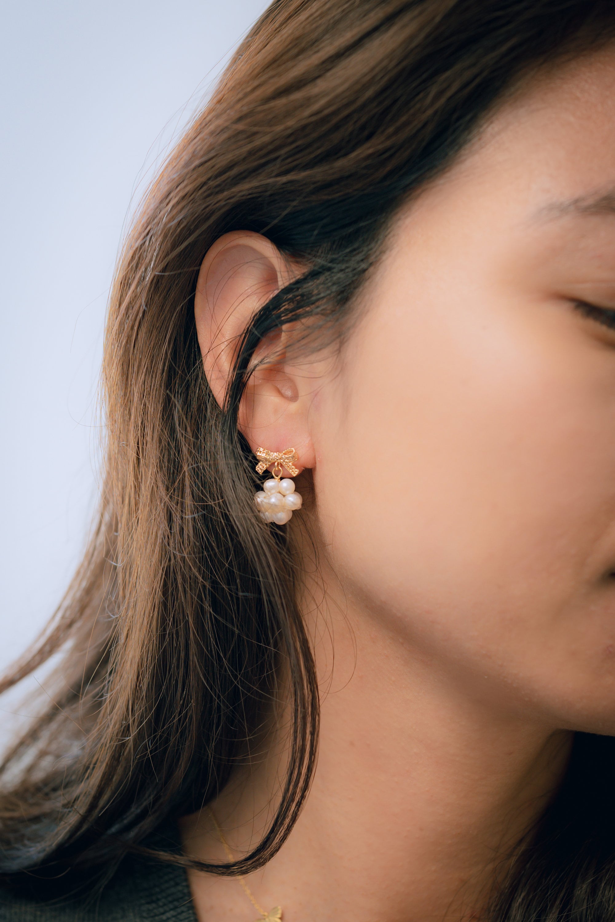 A woman wearing Caellia 14K gold bowknot earrings with dangling freshwater pearl clusters.
