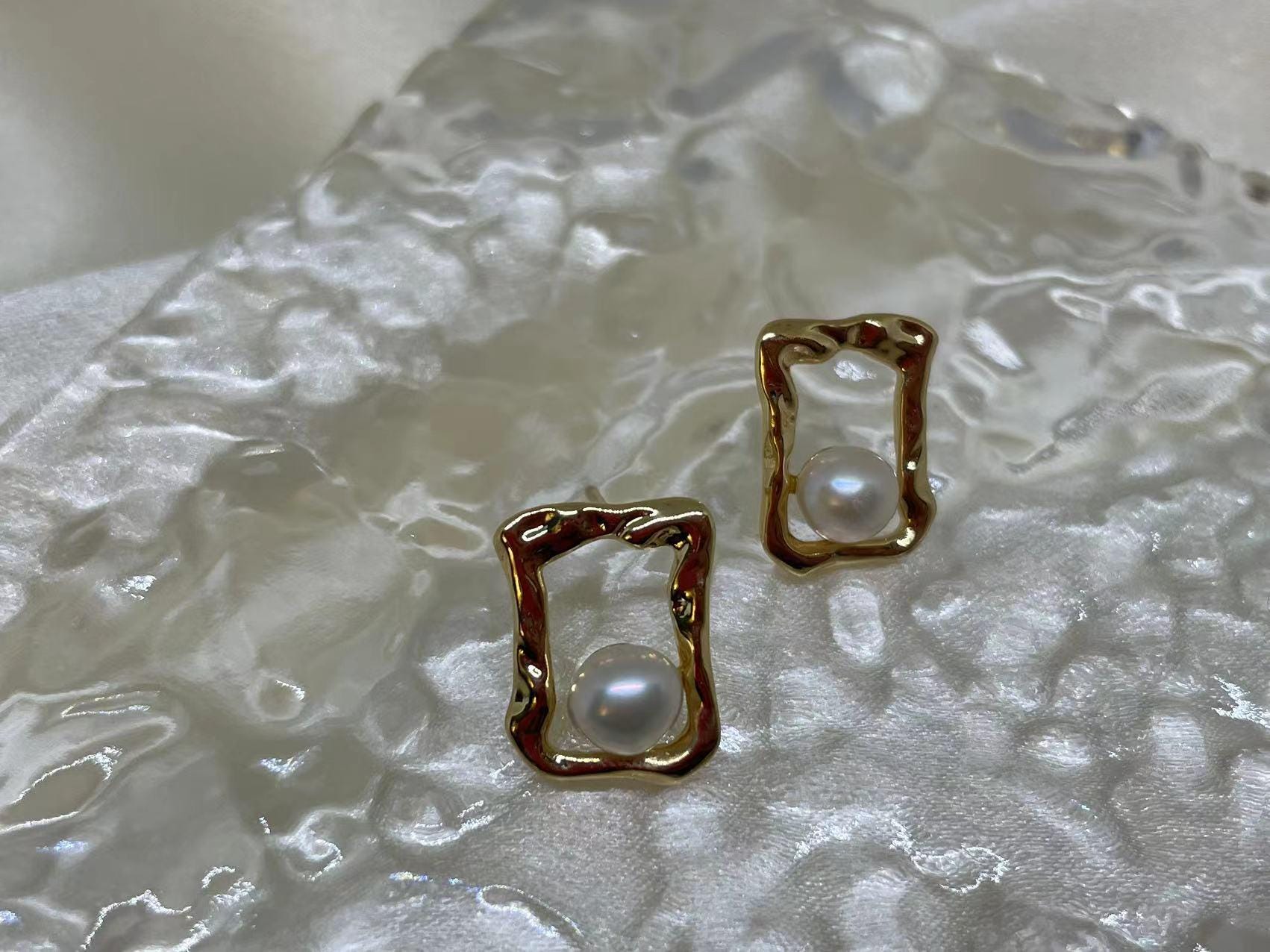 CAELLIA gold plated stud earrings featuring a lustrous freshwater pearl in a textured square frame.