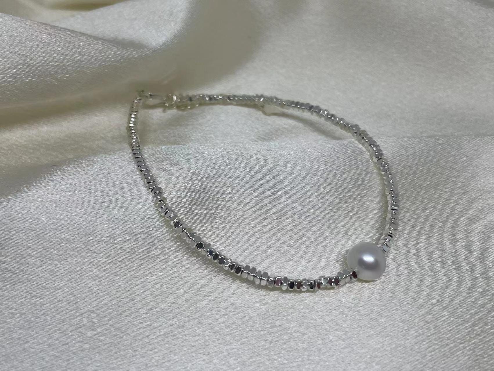CAELLIA freshwater pearl bracelet on a 925 sterling silver chain resting on white fabric.
