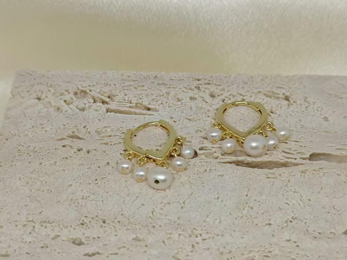 Caellia 14K gold huggie hoop earrings adorned with delicate freshwater pearls.