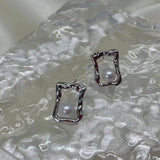 CAELLIA silver stud earrings featuring a lustrous freshwater pearl inside a textured square frame.
