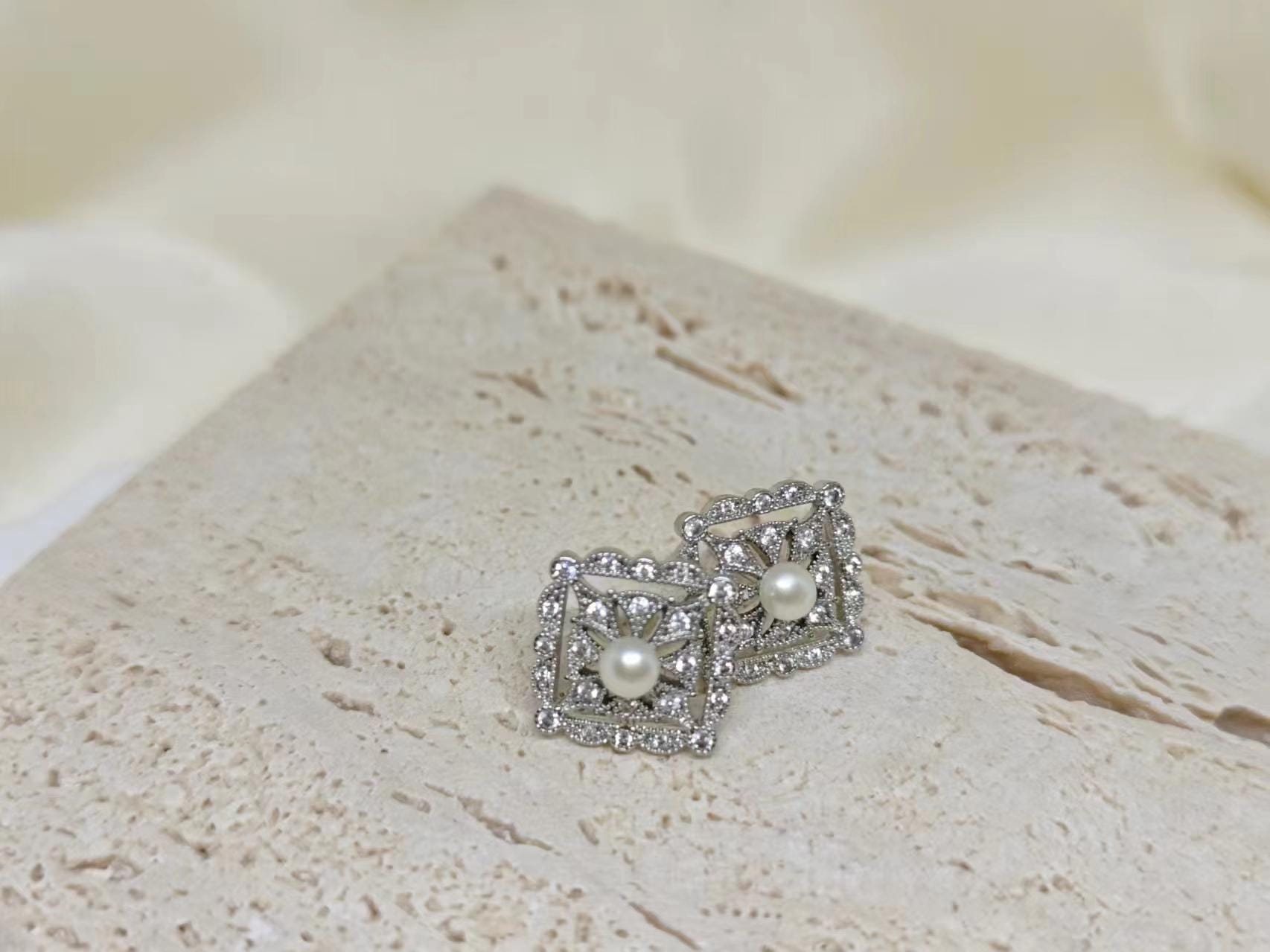 CAELLIA sterling silver square stud earrings featuring a central freshwater pearl and diamond accents.