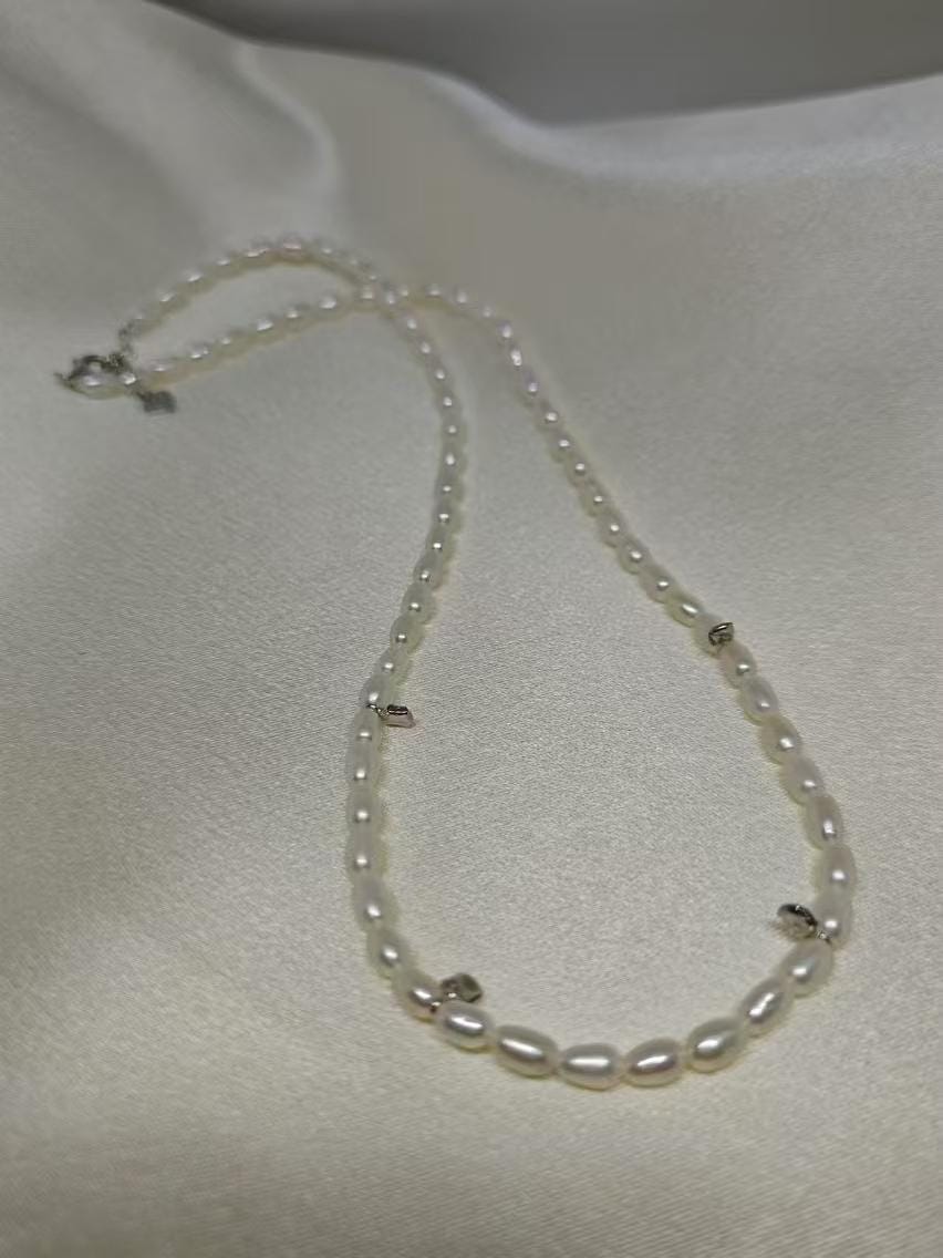 A CAELLIA freshwater pearl bead necklace with small silver accents on a white fabric background.