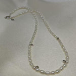 A CAELLIA freshwater pearl bead necklace with small silver accents on a white fabric background.