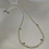 A CAELLIA freshwater pearl bead necklace with small silver accents on a white fabric background.