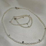 A Caellia freshwater pearl necklace and matching bracelet with silver accents on a white fabric.