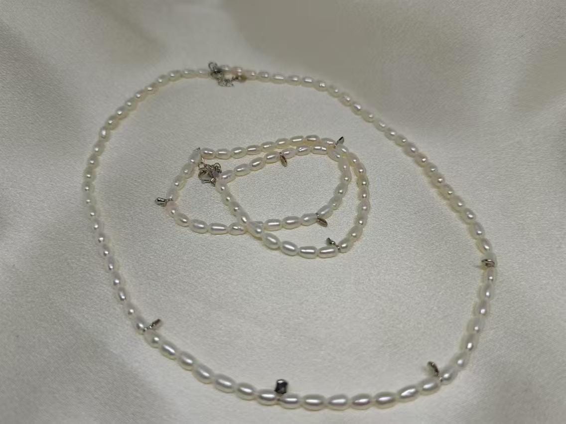 A Caellia freshwater pearl necklace and matching bracelet with silver accents on a white fabric.