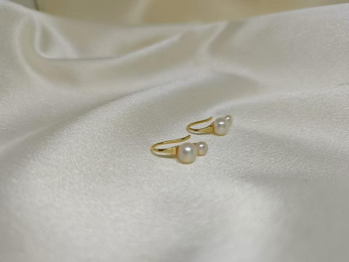 Caellia 18K gold plated stud earrings featuring lustrous freshwater pearls on a white fabric.
