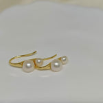 Caellia 18K gold plated stud earrings featuring two freshwater pearls on a curved gold bar.