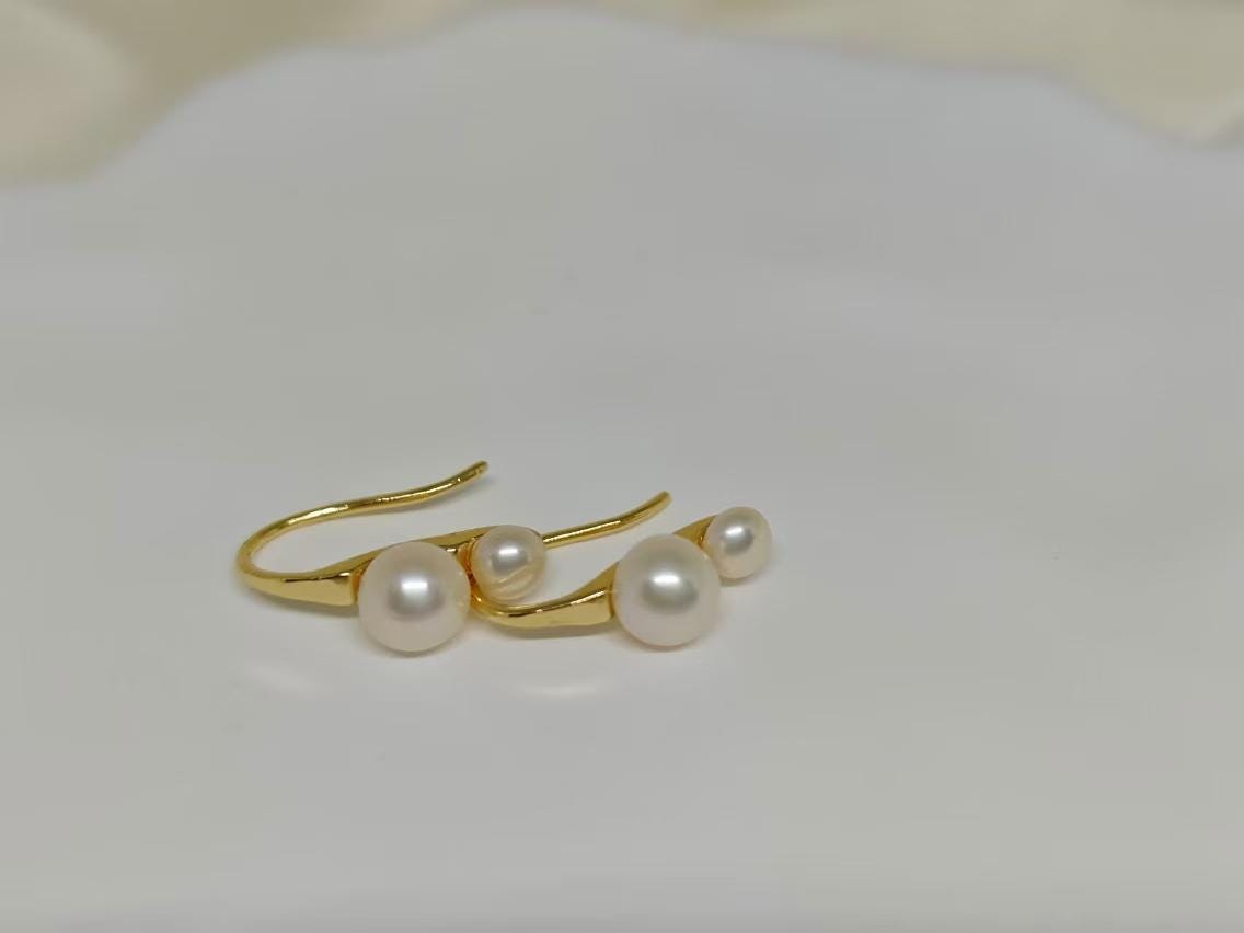 Caellia 18K gold plated stud earrings featuring two freshwater pearls on a curved gold bar.