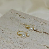 Caellia 18K gold plated stud earrings featuring two freshwater pearls on a textured stone surface.