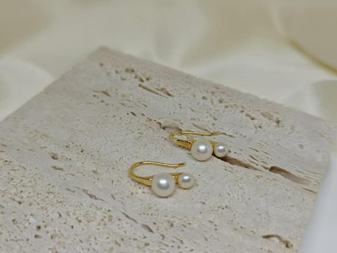 Caellia 18K gold plated stud earrings featuring two freshwater pearls on a textured stone surface.