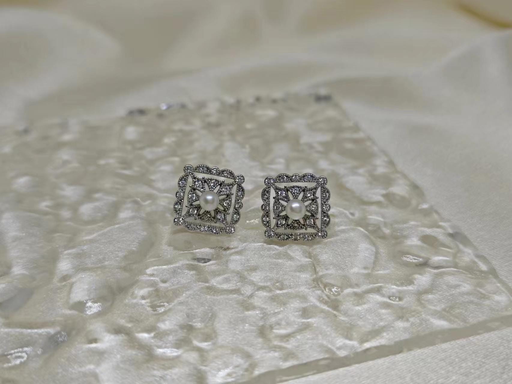 CAELLIA sterling silver square stud earrings featuring a central freshwater pearl and diamond accents.