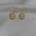 CAELLIA gold plated freshwater pearl stud earrings with a circular frame on a white fabric background.