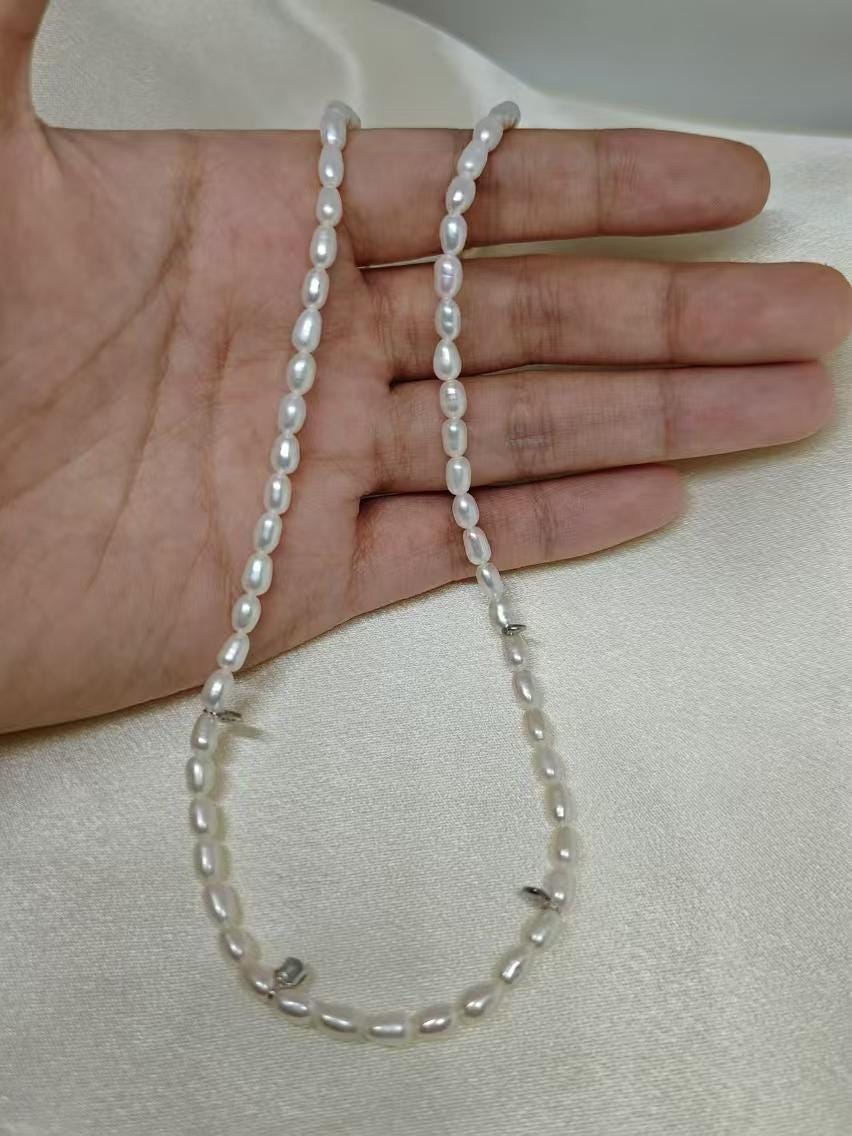 A hand holding a Caellia freshwater pearl necklace with small white beads on a silk background.