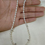 A hand holding a Caellia freshwater pearl necklace with small white beads on a silk background.