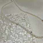 A delicate Caellia freshwater pearl necklace with a sterling silver clasp on a textured surface.