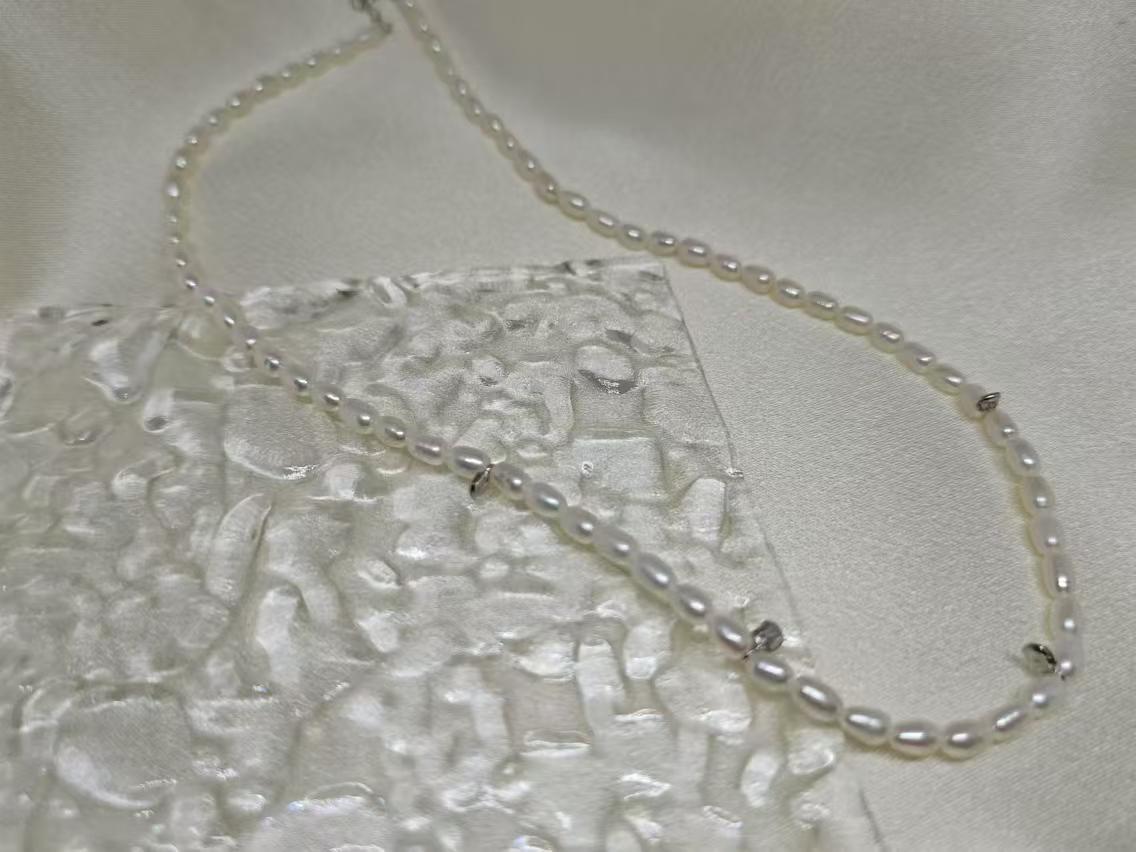A delicate Caellia freshwater pearl necklace with a sterling silver clasp on a textured surface.