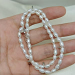 CAELLIA double wrapped freshwater pearl bracelet with sterling silver accents held in a hand.