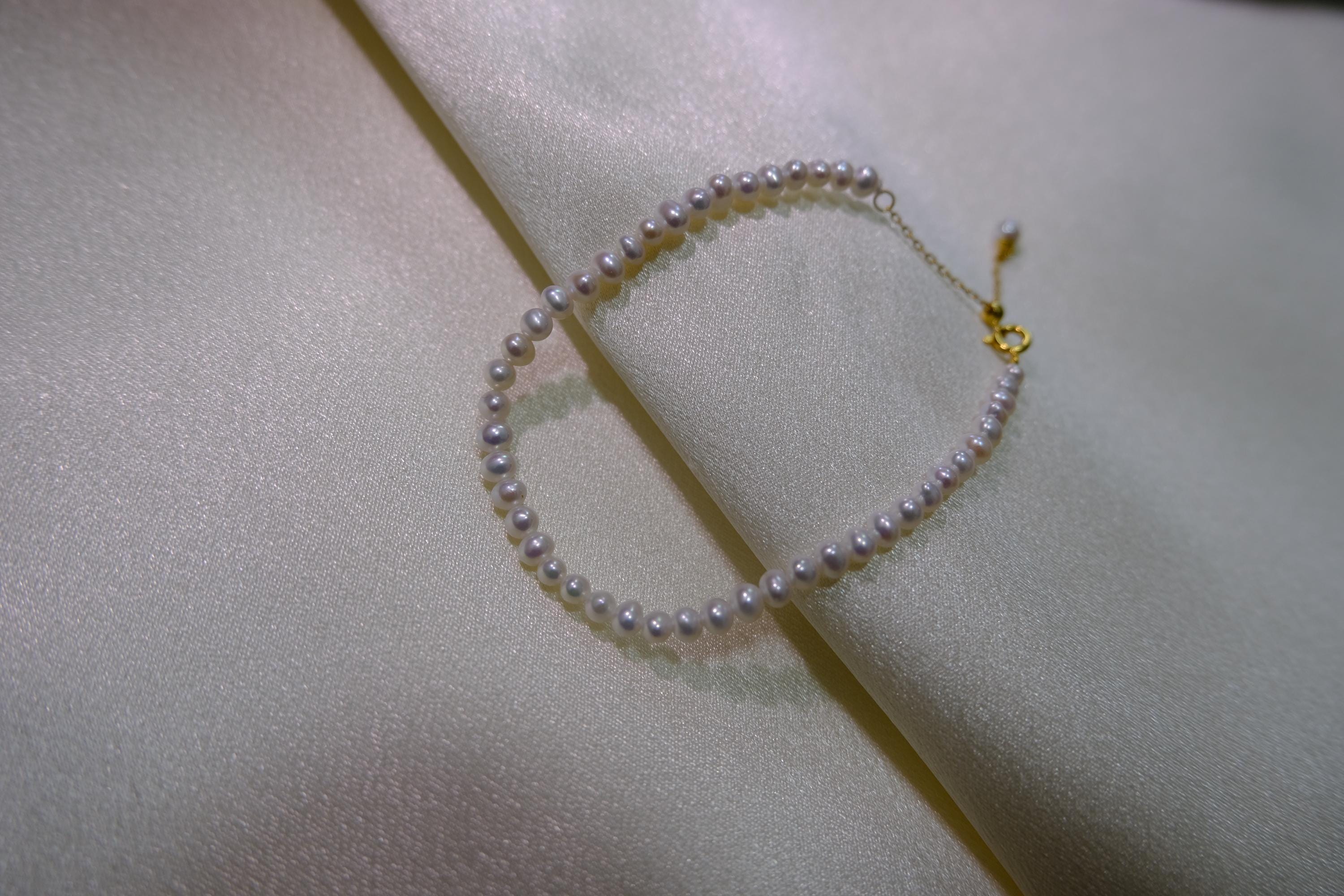 CAELLIA freshwater pearl bracelet with gold plated sterling silver hardware on white fabric.