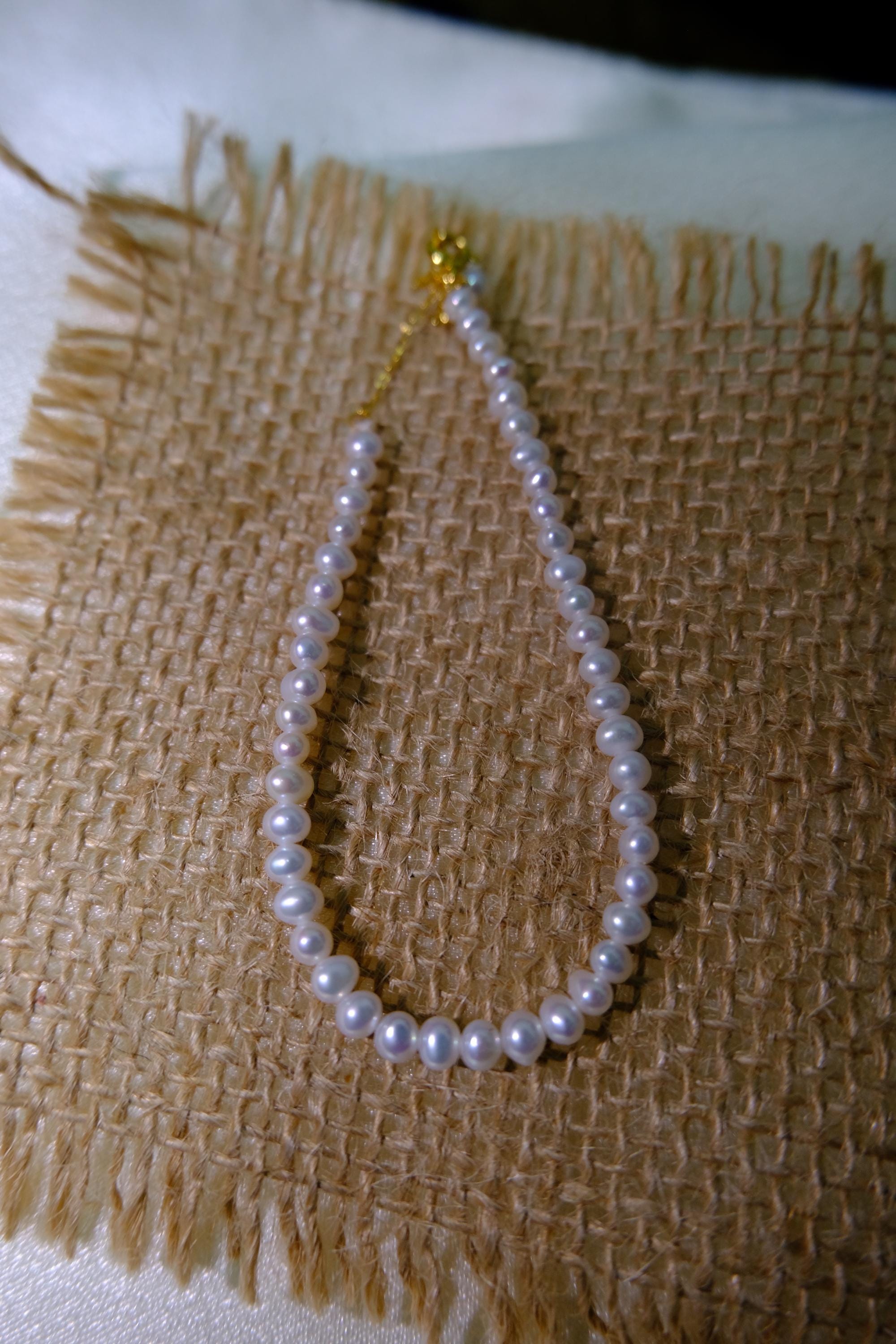 CAELLIA freshwater pearl bracelet with gold plated sterling silver hardware on a burlap background.